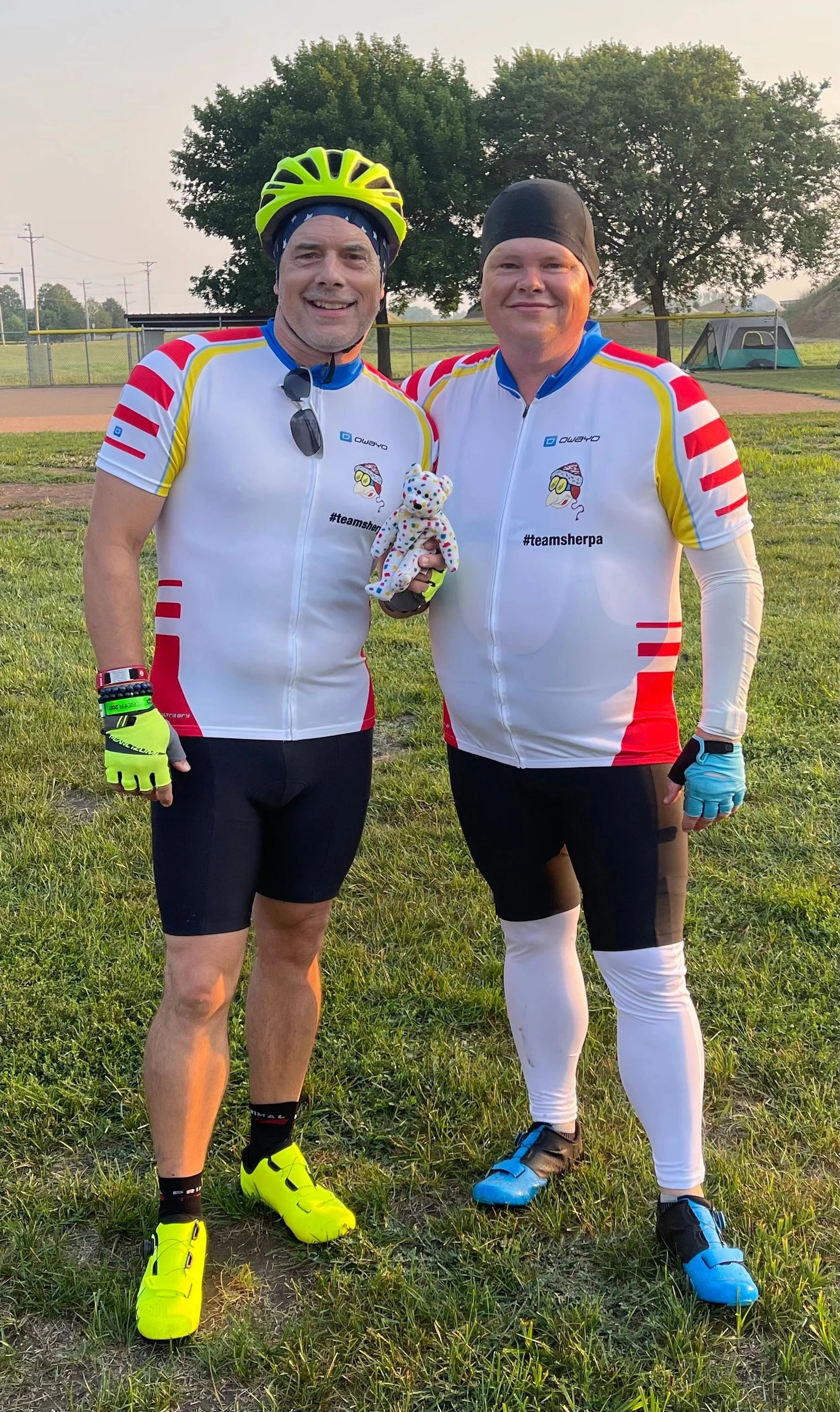 Two riders in #teamsherpa kit at a ballfield campsite