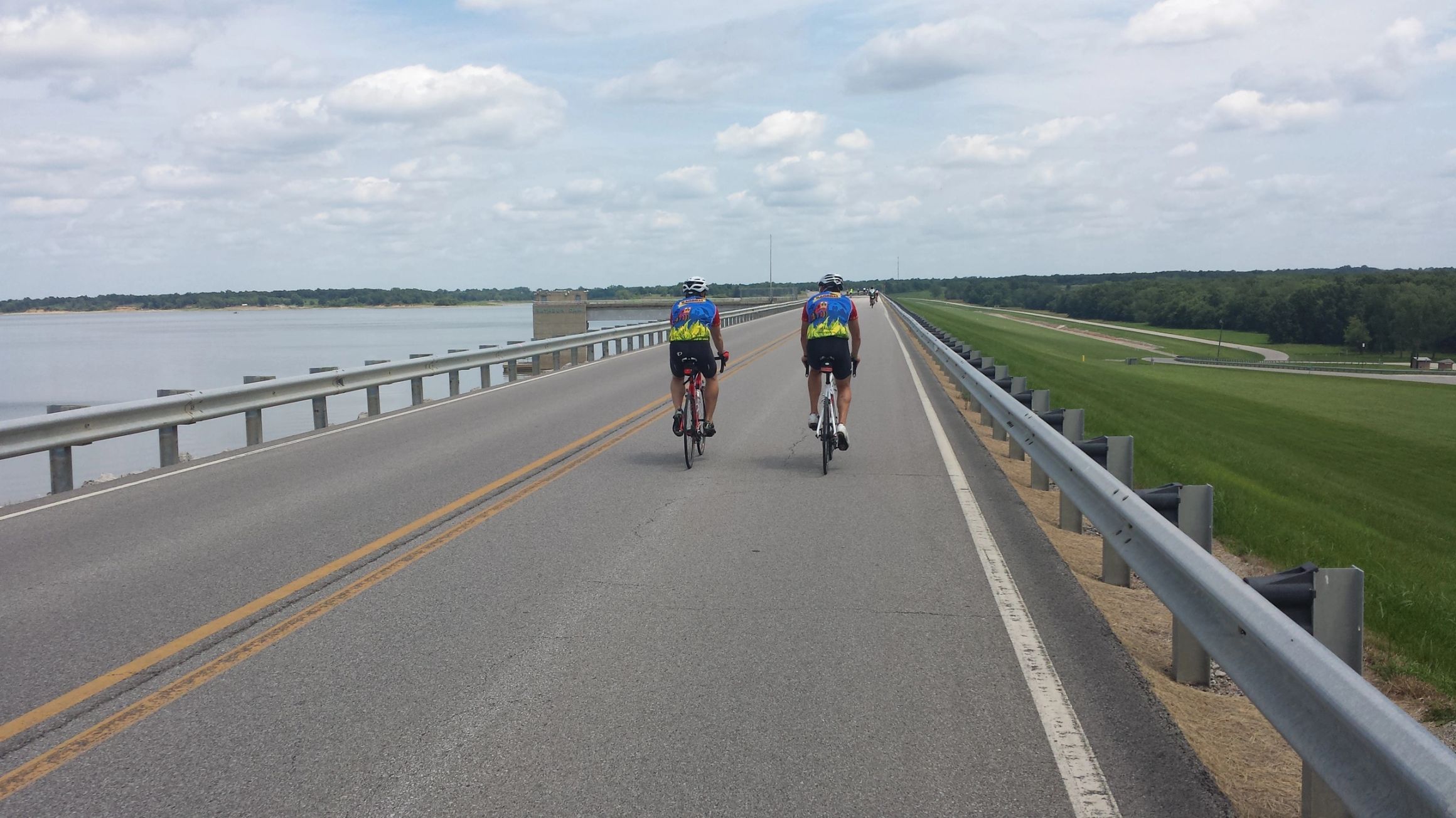 Two riders crossing a causeway over a reservoir